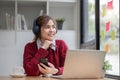 Asian female college student using laptop and phone with headphones while studying. Reading messages and greeting Royalty Free Stock Photo