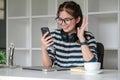 Asian female college student using laptop and phone with headphones while studying. Reading messages and greeting Royalty Free Stock Photo