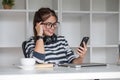 Asian female college student using laptop and phone with headphones while studying. Reading messages and greeting Royalty Free Stock Photo