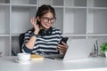 Asian female college student using laptop and phone with headphones while studying. Reading messages and greeting Royalty Free Stock Photo