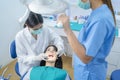 Asian female dentist adjust dental surgical light then starts checking or examining tooth of young girl patient lying on dental ch