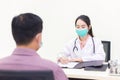 Asian female doctor is inquiring about a male patient`s illness. In the hospital examination room, she wears medical face mask Royalty Free Stock Photo