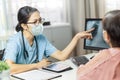 Asian female doctor in medical mask examining and pointing to radiological chest X-ray film on monitor computer with Elderly woman Royalty Free Stock Photo