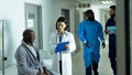 Asian female doctor and smiling senior african american male patient talking in hospital corridor Royalty Free Stock Photo