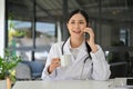 Asian female doctor talking on her smartphone and sipping coffee during her coffee break Royalty Free Stock Photo