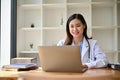 An Asian female doctor in a uniform using her laptop at her desk in her office Royalty Free Stock Photo