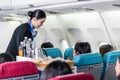 Asian female flight attendant serving food and drink to passengers on airplane. The cabin crew pushing the cart on aisle to serve