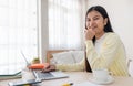 Asian female freelancer reading report on laptop and jot down note on table in bedroom at home.Work at home concept.work from home