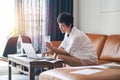 Asian female freelancer sitting on couch drinking water & working on laptop at home Royalty Free Stock Photo