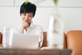 Asian female freelancer sitting on couch smiling & working on laptop at home Royalty Free Stock Photo