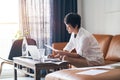 Asian female freelancer sitting on couch thinking & working on laptop at home Royalty Free Stock Photo