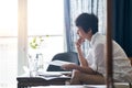 Asian woman sitting on couch thinking & working on laptop at home