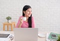 Asian female freelancer smile and drink coffee with relax emotion and looking out of window take breake from laptop work on