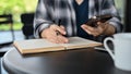 An Asian female freelancer using her smartphone and taking notes on her notebook Royalty Free Stock Photo