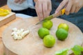 Asian female holds orange knife to slide green lemon lime on the wood circle plate with garlice beside Royalty Free Stock Photo