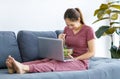 Millennial Asian female housewife sitting on cozy sofa couch in living room at home eating fresh organic vegetable salad from Royalty Free Stock Photo