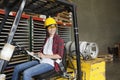 Asian female industrial worker with clipboard looking away while sitting in forklift truck