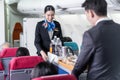 Asian female and male flight attendant serving food and drink to passengers on airplane. The cabin crew pushing the cart on aisle Royalty Free Stock Photo