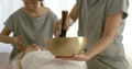 Asian female masters are massaging face of client woman and making vibrations by tibetan bowl