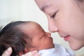 Asian female parent holding newborn baby with care on bed at hospital. mother kissing baby. nose touching.