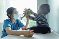 Asian female Pediatrician doctor wearing protective face mask playing dinosaur doll with her little baby boy patient before Royalty Free Stock Photo