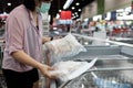 Asian female people choosing frozen seafood purchases frozen cut fish packages with fish in freezer in food department of