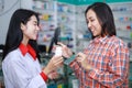 Asian female pharmacist smiling and selling vitamins and medicines capsule to the customer in pharmacy shop thailand