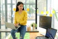 Asian female programmer for yellow shirt sit on the shelf and place laptop on leg.She stared at computer screen on the table and