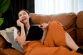 Asian female relaxes on sofa living room while reading a book and talking on the phone Royalty Free Stock Photo