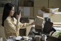 Asian female small business owner using mobile app on smartphone checking parcel box. Warehouse worker, seller holding phone scann Royalty Free Stock Photo