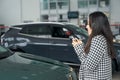 Asian female stands in a car dealership with car keys