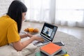Asian female student video conference with teacher and friends using e-learing app on laptop computer at home.woman lying down on