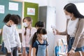 Asian Female Teacher measuring temperature of Multi-ethnic group of students standing in a queue in classroom at Elementary school Royalty Free Stock Photo