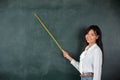 Asian female teacher smiling with wooden stick pointing to blackboard