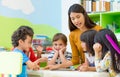 Asian female teacher teaching mixed race kids reading book in cl