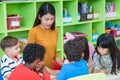 Asian female teacher teaching mixed race kids reading book in cl Royalty Free Stock Photo