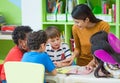 Asian female teacher teaching mixed race kids reading book in cl Royalty Free Stock Photo