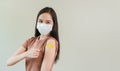 Asian female thumbs up wearing mask with showing plaster on shoulder after covid-19 vaccine Injection.