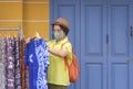 Asian female tourist in vintage style and protective face mask choosing tie dye t-shirt on cloth rack of street clothing store Royalty Free Stock Photo