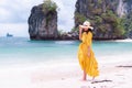 Asian female tourist in yellow dress walks on white sand beach at Hong Island, Krabi sea, Thailand