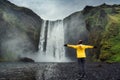 Asian female tourist in yellow jacket enjoying the Skogafoss waterfall flowing from cliff on summer in Iceland