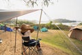 Asian female tourists sit on camping chairs, relax and have fun, camping with mountain and river views. Afternoon sunshine