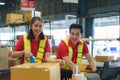 Asian female worker packing cardboard box with tape gun dispenser in warehouse. Thai employee packing goods in large industrial Royalty Free Stock Photo