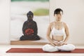 Asian female yoga meditation lotus pose with buddha artwork, mindfulness wellbeing meditation concept