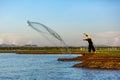 Asian Fisherman throwing a net for catching freshwater fish in the early morning