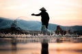 Asian fisherman on wooden boat casting a net for catching freshwater fish Royalty Free Stock Photo