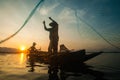 Asian fisherman on wooden boat casting a net for catching freshwater fish Royalty Free Stock Photo