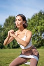 Asian fitness girl doing squats in park, using resistance band, stretching yoga rope for workout training on fresh air Royalty Free Stock Photo