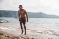 Asian fitness guy doing jumping jacks, star jump or burpees exercise at seaside outdoors. Healthy lifestyle by the beach