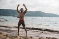 Asian fitness guy doing jumping jacks, star jump or burpees exercise at seaside outdoors. Healthy lifestyle by the beach